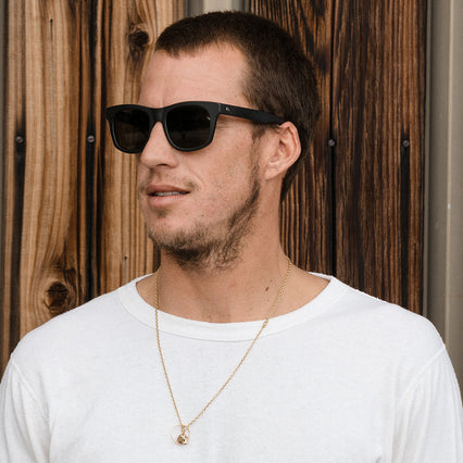 Man wearing matte black sunglass with grey polarized lenses and classic wayfarer shape.